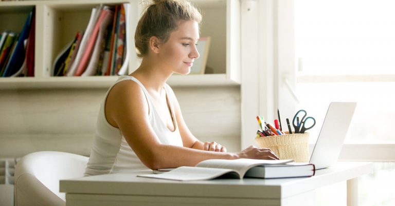 A young woman works at her desk in her dorm room.