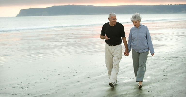 An elderly couple walk along a beach front.