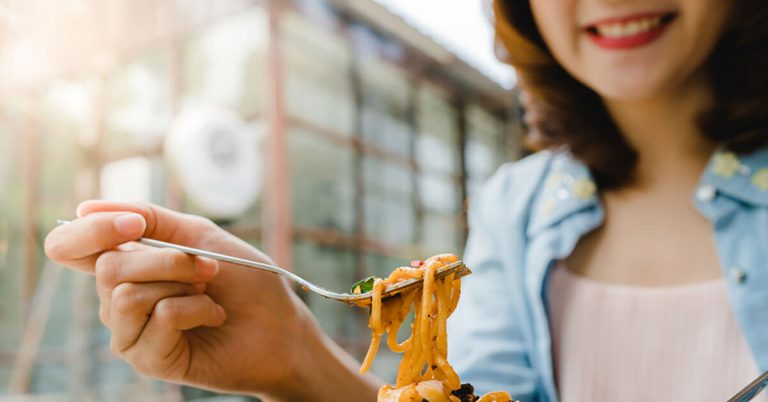 A close-up shot of a woman eating a plate of pasta